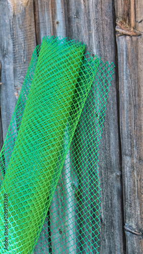 Close-up of a roll of green garden plastic mesh against a background of old vertical barn wood planks.