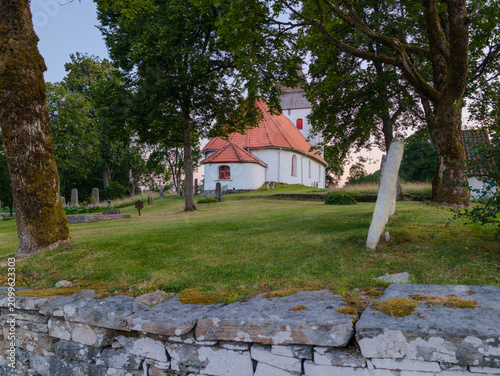 Foto Old Hyssna Church surrounded by trees and historic churchyard in Västra Götaland