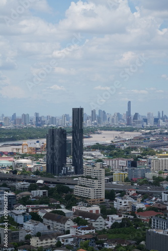 A wide view over a dense modern city packed with skyscrapers and office towers over the capital of Thailand in Southeast Asia, under a bright clear sky, in warm daylight with crisp detail.