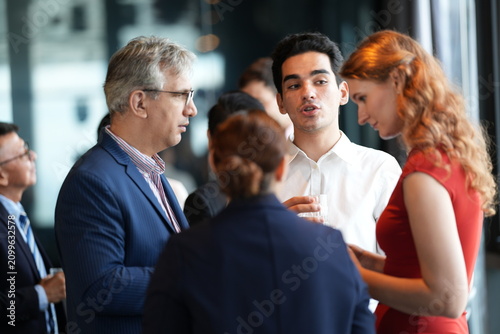 Bild auf Leinwand Guests with drinks at a hotel event, mingling and laughing at the reception at a bright hotel reception by the windows, in a stylish contemporary hospitality setting