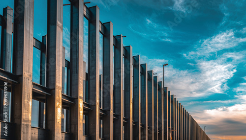 A modern building with vertical metal panels and large glass windows, set against a partly cloudy sky during sunset, showcasing contemporary architecture design.