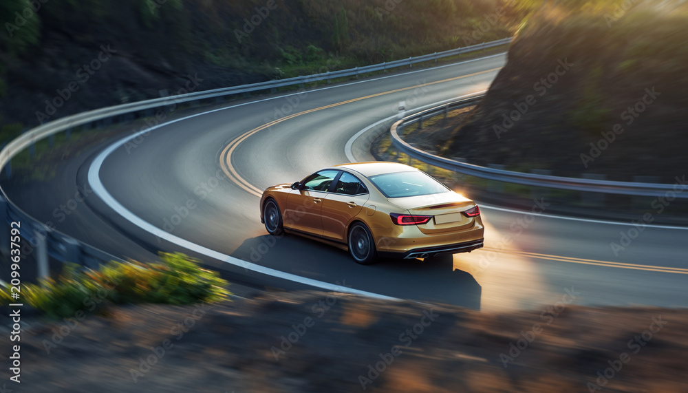 Naklejka premium A sleek, modern sedan driving along a winding mountain road during sunset, with guardrails and trees on the roadside, creating a scenic and dynamic landscape.