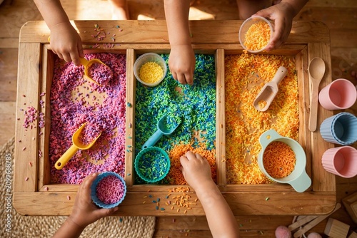 Children playing with colorful sensory rice in a wooden activity table.