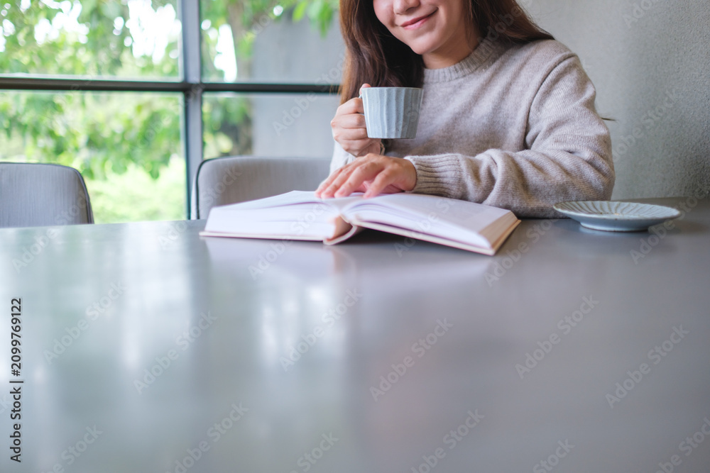 Obraz premium Closeup image of a woman reading a book and drinking coffee