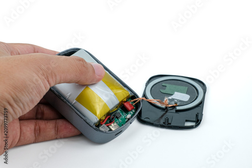 A hand opens a damaged power bank with a swollen lithium battery and exposed internal wiring on a white background. Suitable for swollen battery, power bank repair, lithium battery failure
