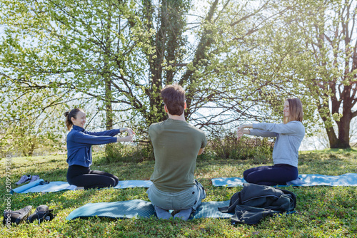 Three Friends Practicing Outdoor Stretching on Yoga Mats in a Sunny Park