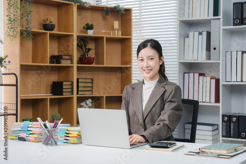 Cheerful business lady working on laptop in office, Asian happy beautiful businesswoman in formal suit work in workplace. Attractive female employee office worker smile