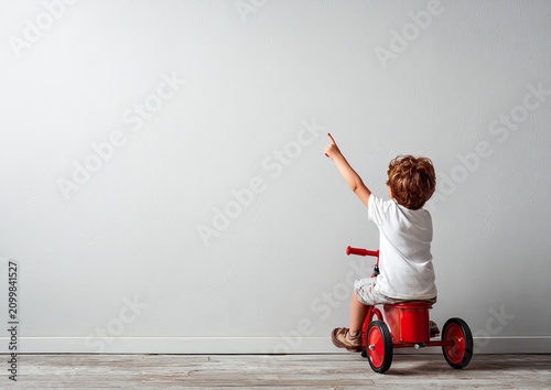 Child Points Up from Red Tricycle on Floor
