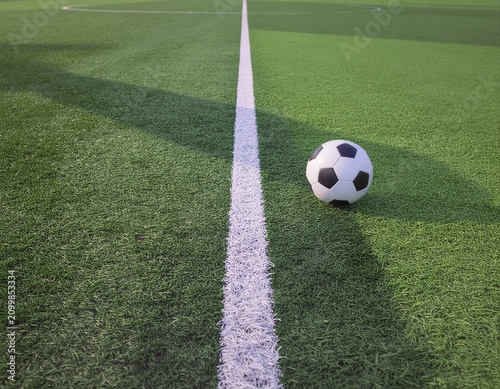 Soccer ball centered on a white field line on an artificial turf pitch with a top-down perspective