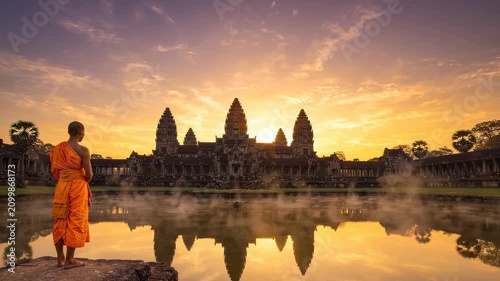 Ancient lotus-tower temple in Cambodia reflected in a still pool at sunrise, a saffron-robed monk standing silently at the water's edge
