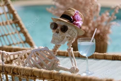 A skeleton wearing sunglasses and a hat by the pool. Concept: end of summer, close of summer season, change of season, beginning of fall, early fall.