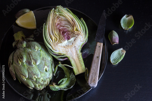 Foto Fresh artichokes cut half with lemon and knife - dark and moody tone