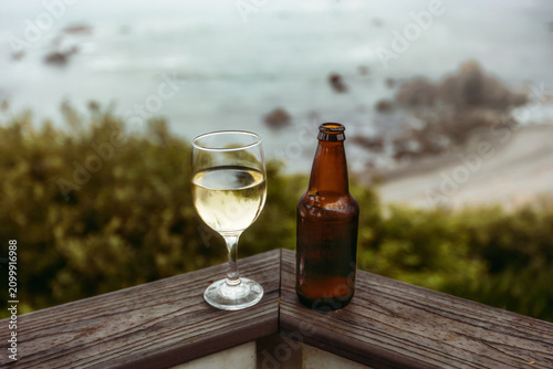 Fotografía A glass of white wine and a beer bottle sit on a deck