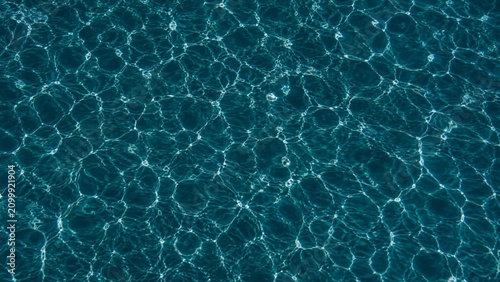 A high contrast aerial shot of dark teal pool water with bright silver caustic streaks.
