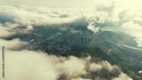 Aerial view of city buildings surrounded by green mountains and moving white clouds