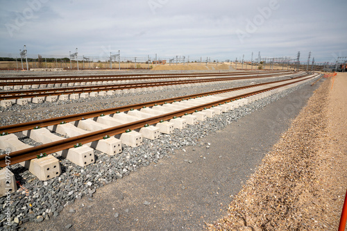 Curved railway tracks with concrete sleepers and new gravel ballast under clouds.