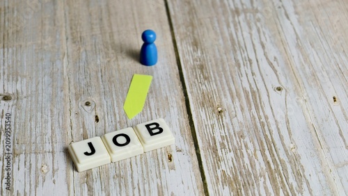 Blue pawn figure pointing towards letter tiles spelling JOB on a wooden background.