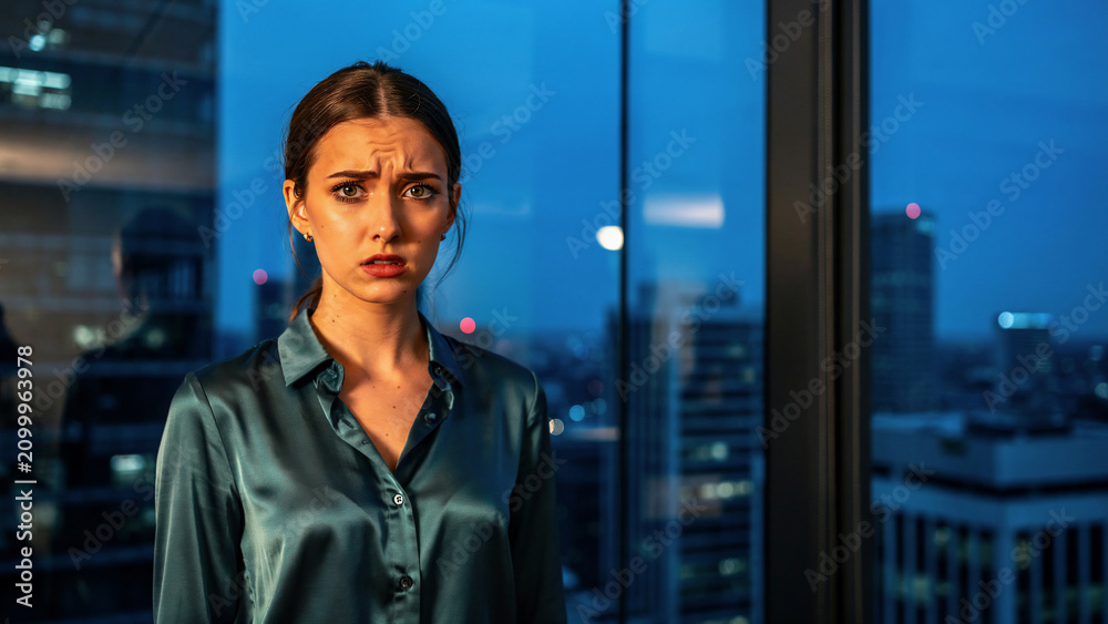 Fototapeta premium Worried woman with furrowed brow looking at camera, dark blue satin shirt, concept for stress, business pressure and emotional burden