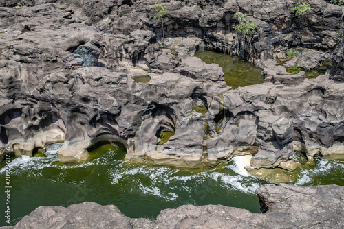 A high-angle shot of the naturally formed basalt rock potholes, locally known as Ranjan Khalge, carved over centuries by the Kukadi River in Nighoj, Ahmednagar district, Maharashtra, India.
