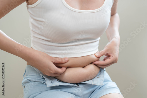 Cuadro en lienzo Close-up of a young woman pinching belly fat on her stomach in white crop top