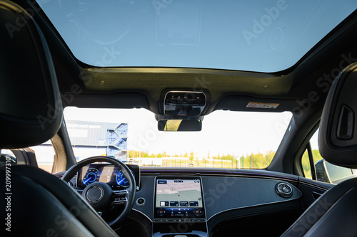 Panoramic sunroof and front dashboard view inside a modern luxury car cabin from the back seat, close up.