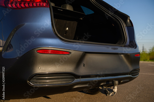 Rear bumper of a modern luxury electric car featuring parking sensors, a tow hitch, and an open trunk, close up.