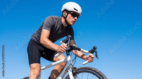 Male cyclist riding white road bicycle against clear blue sky on sunny day