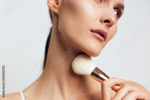 Foto Young woman with smooth skin gently applies powder makeup on her neck using a large brush in a bright studio setting with a white background and soft lighting
