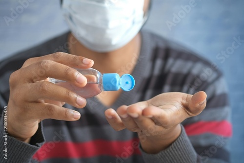 Tablou pe pânză Man in medical face mask applying antibacterial hand sanitizer gel from bottle