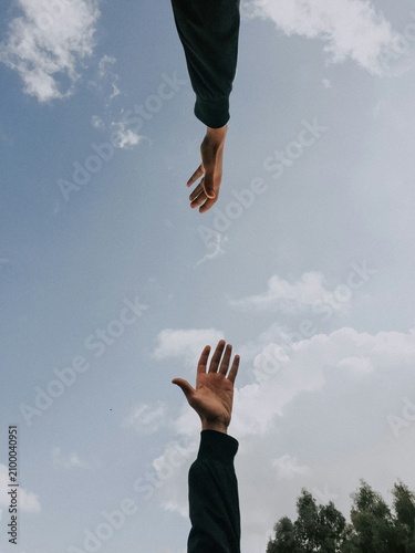 Two hands reaching out toward each other under blue sky for assistance concept