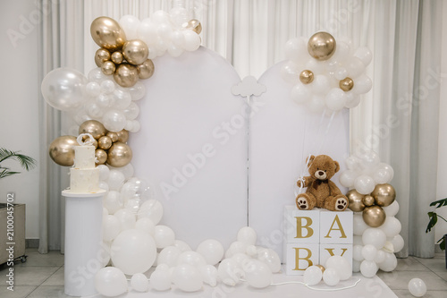 Arch. Beautiful photo zone for a birthday, baptism, or baby shower, featuring white arched panels, white and gold balloon garlands, a teddy bear on 