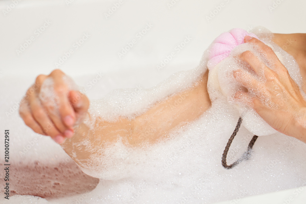 Fototapeta premium Woman washing arm with loofah in bubble bath