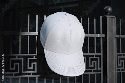 White cap hanging on metal fence with dark background for mockup template