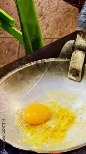 Fresh egg mixture cooks in a metal pan over charcoal during traditional Indonesian street food preparation.