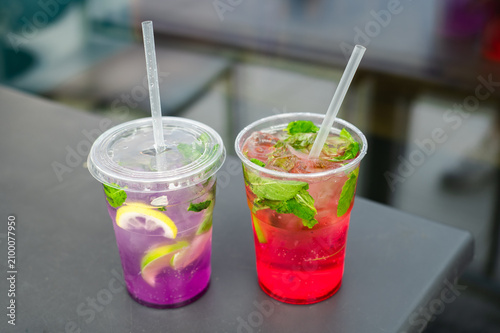 Colorful summer lemonades in takeaway cups. Two refreshing homemade lemonades served in plastic takeaway cups with ice, fresh fruit and mint. Cold summer beverages and outdoor refreshment.