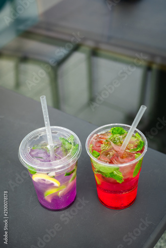 Two colorful iced lemonades on an outdoor table. Refreshing fruit lemonades with fresh mint, citrus slices and ice in transparent plastic cups. Summer beverage concept.