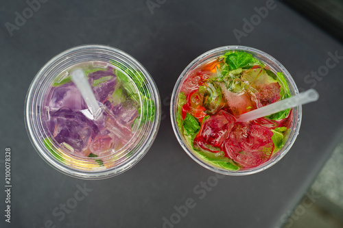 Top view of colorful fruit lemonades. Overhead view of two refreshing homemade lemonades with fresh fruit, mint and ice. Cold summer drinks served in takeaway cups.