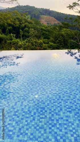 Blue infinity pool overlooks lush forested hills at a tranquil tropical mountain resort.