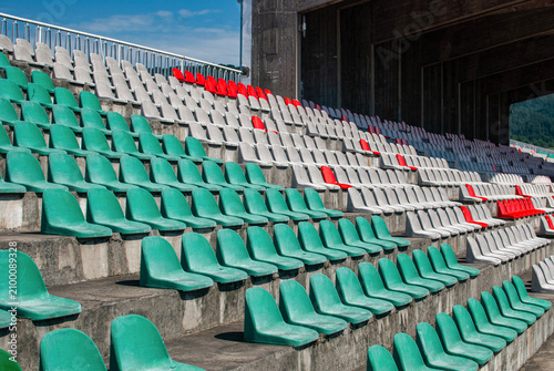 Empty grandstand with colorful spectator seats in a community sports stadium on a sunny summer day.