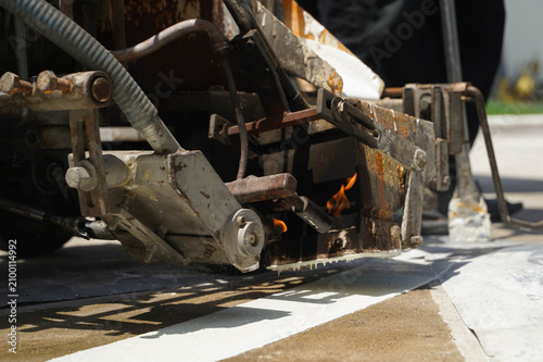 Workers using a professional road marking machine to apply hot thermoplastic paint on a concrete surface for traffic line striping.