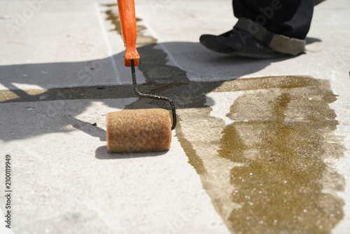 Construction worker applying primer glue on concrete road surface before