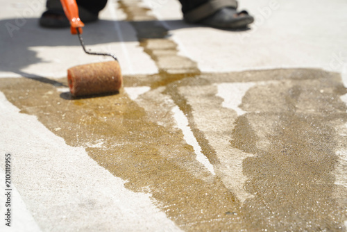 Construction worker applying primer glue on concrete road surface before