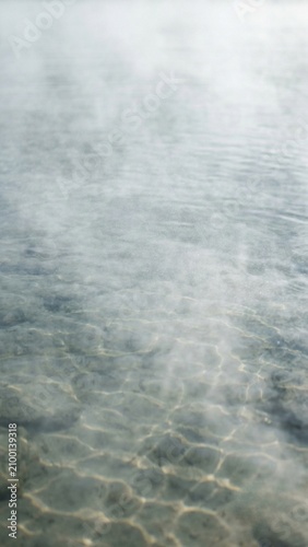 A clear water surface with soft hovering mist close to the surface, vertical 9:16 overhead view.