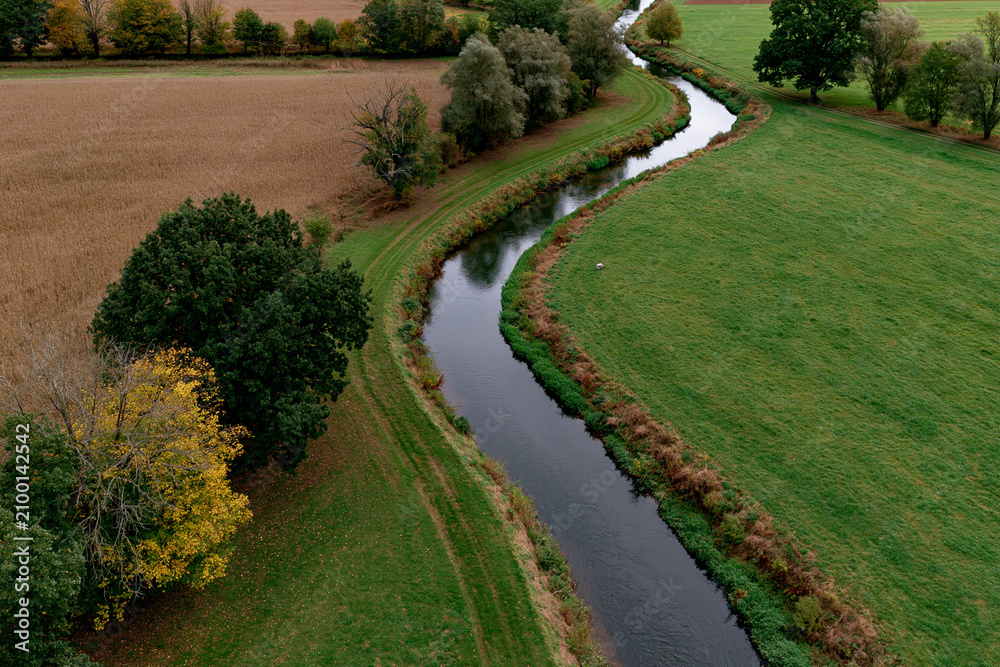 Fototapeta premium River flows through rural fields and trees