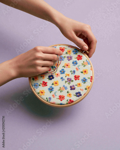 Woman embroidering colorful flowers on canvas using needle and thread in wooden hoop. Handcraft hobby as creative activity. Textile art design for home decor or DIY craft project.