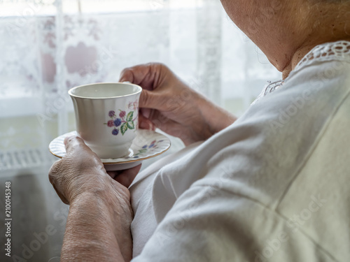Obraz na płótnie Close Up of Senior Woman Holding Floral Tea Cup Near Bright Window