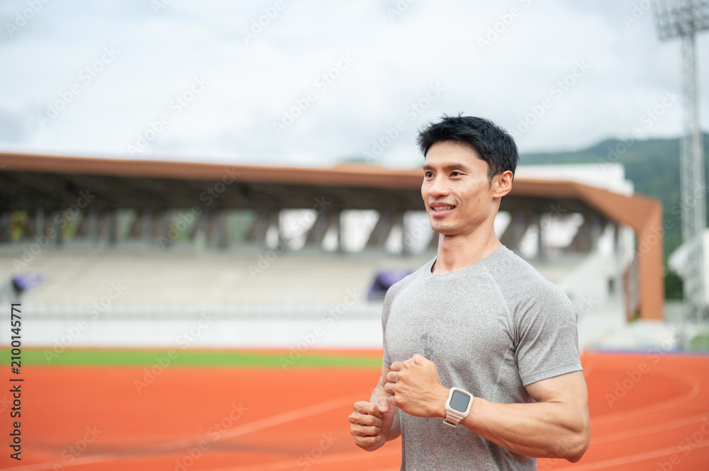 Fototapeta premium Asian athletic man running happily with a smile on track during a workout session in sports stadium.