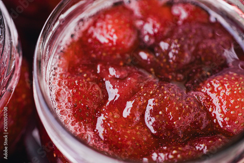 Obraz na plátne Close-up of whole strawberries immersed in glossy red syrup inside an open glass jar, with visible seeds, bubbles, and rich texture
