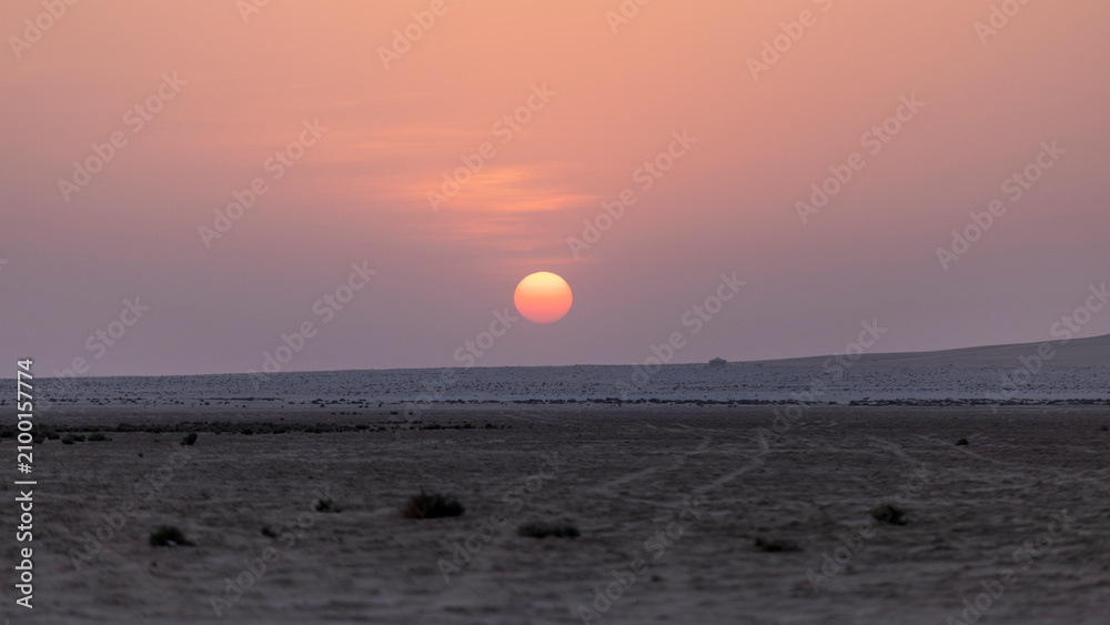 Obraz premium Beautiful pink and purple sunset dipping below a flat desert horizon, creating a serene, minimalist twilight landscape under pastel skies.