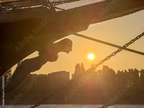 Photography Silhouette of a tall ship figurehead against a golden sunset in Antwerpen, Belgi